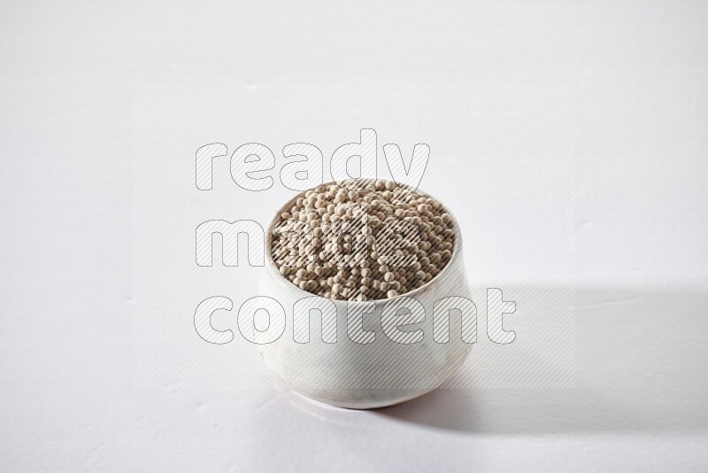 A beige pottery bowl full of white pepper beads on white flooring