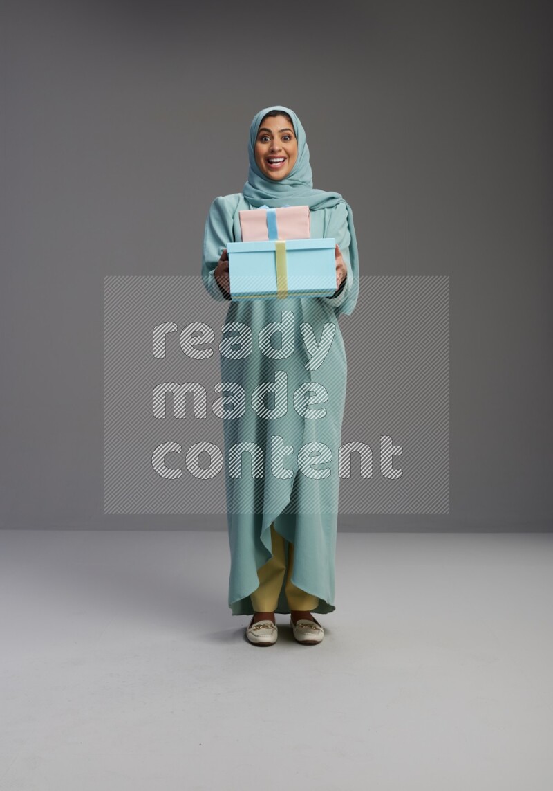 Saudi Woman wearing Abaya standing holding gift box on Gray background
