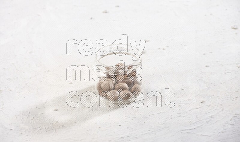 A glass jar full of whole nutmeg seeds on a white flooring