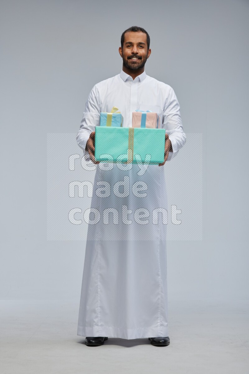 Saudi man Wearing thob standing holding gift box on Gray background