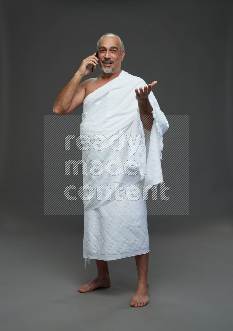 A man wearing Ehram Standing talking on phone on gray background