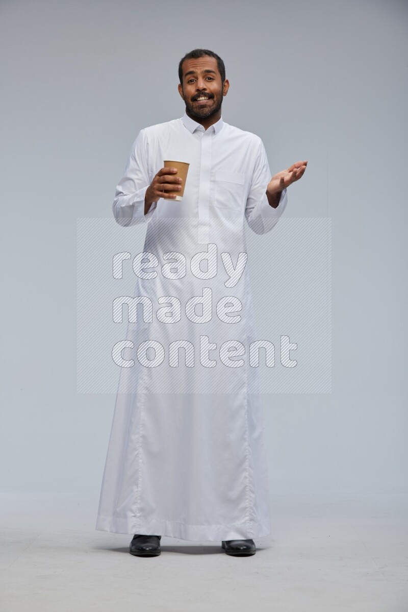 Saudi man wearing thob standing holding paper cup on gray background