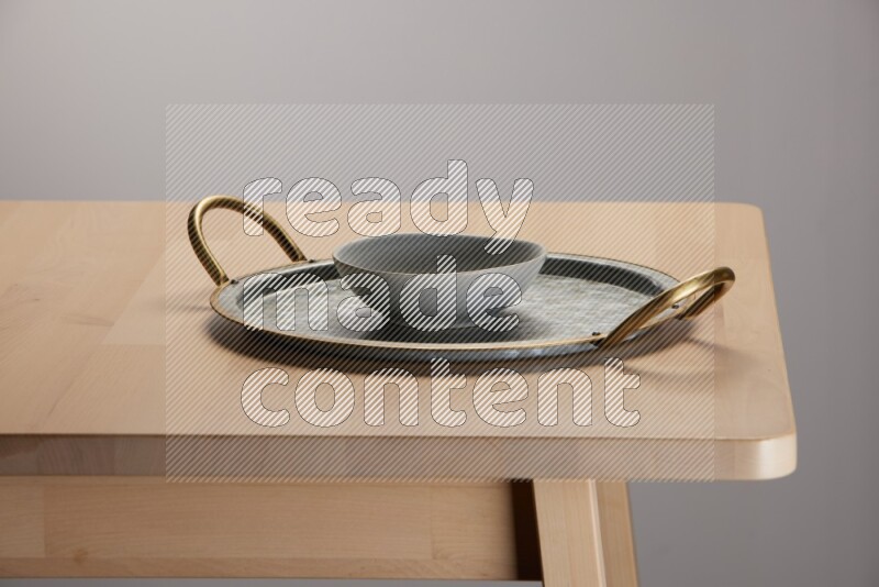 grey bowl placed on a rounded stainless steel tray with golden handels on the edge of wooden table
