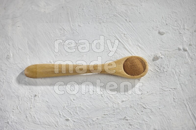 Cinnamon powder in a wooden spoon on a white background