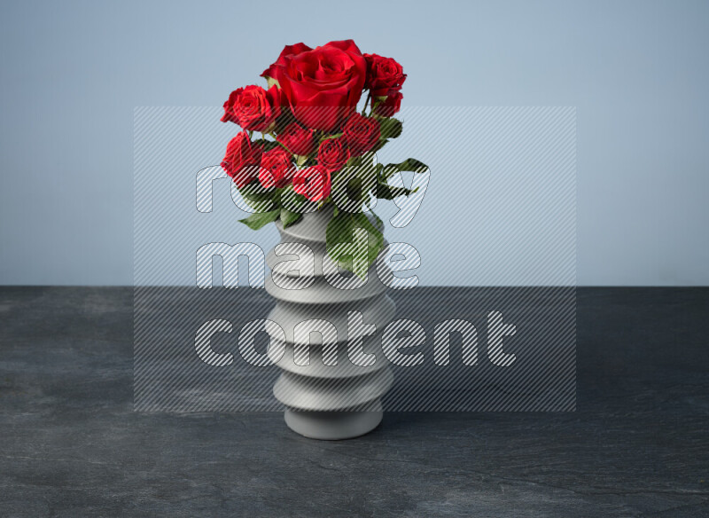 An arrangement of vivid red roses in a grey spiral vase on black marble background