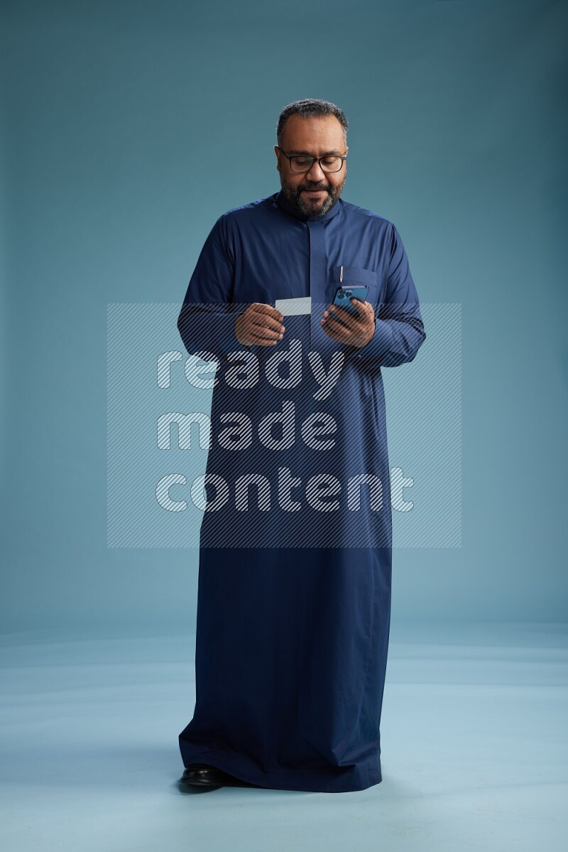 Saudi Man without shimag Standing holding ATM while talking on phone on blue background