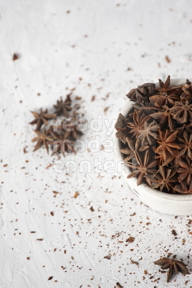 Star Anise in a white bowl and more of it sprinkled on white background