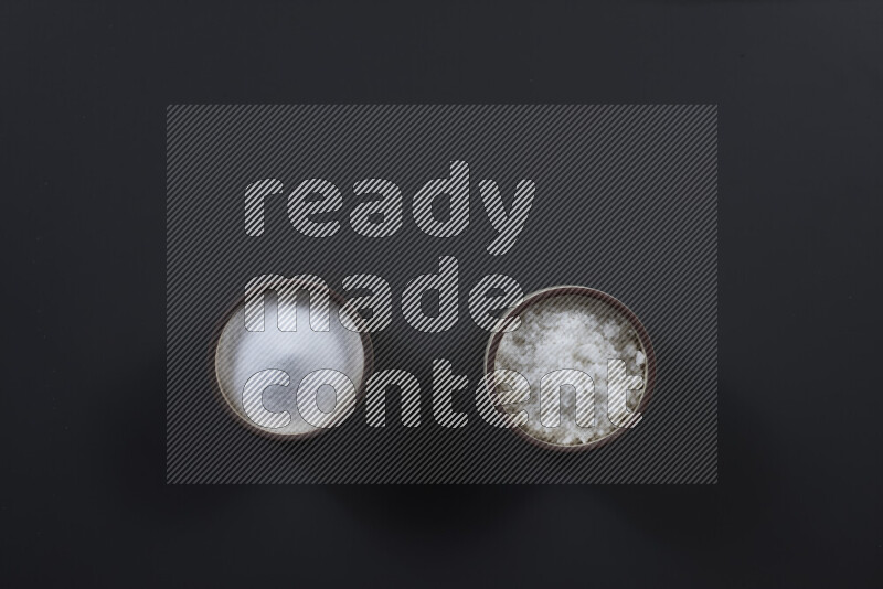 Pottery bowl full of fine table salt and coarse sea salt on black background