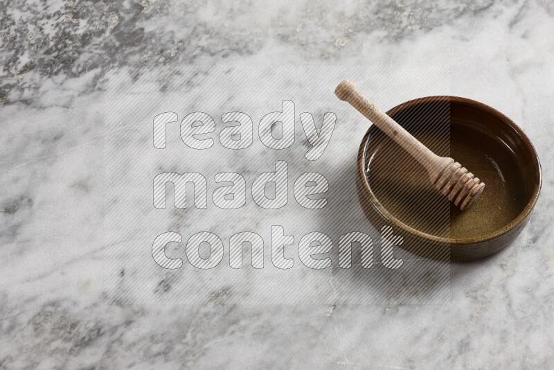Multicolored pottery oven plate with wooden honey dipper in it on grey marble background