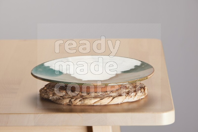 multi-colored pottery Plate placed on a small light colored straw placemat on the edge of wooden table