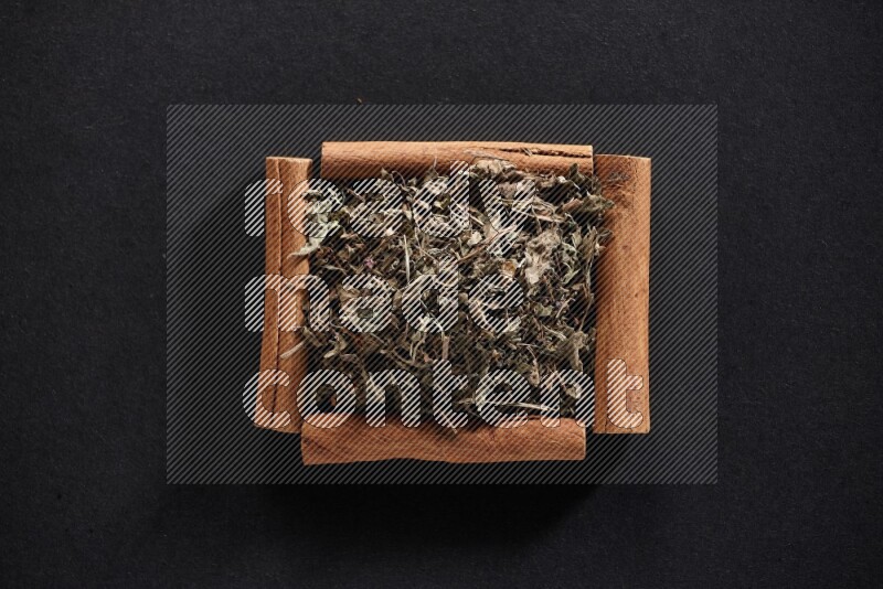 A single square of cinnamon sticks full of dried basil on black flooring