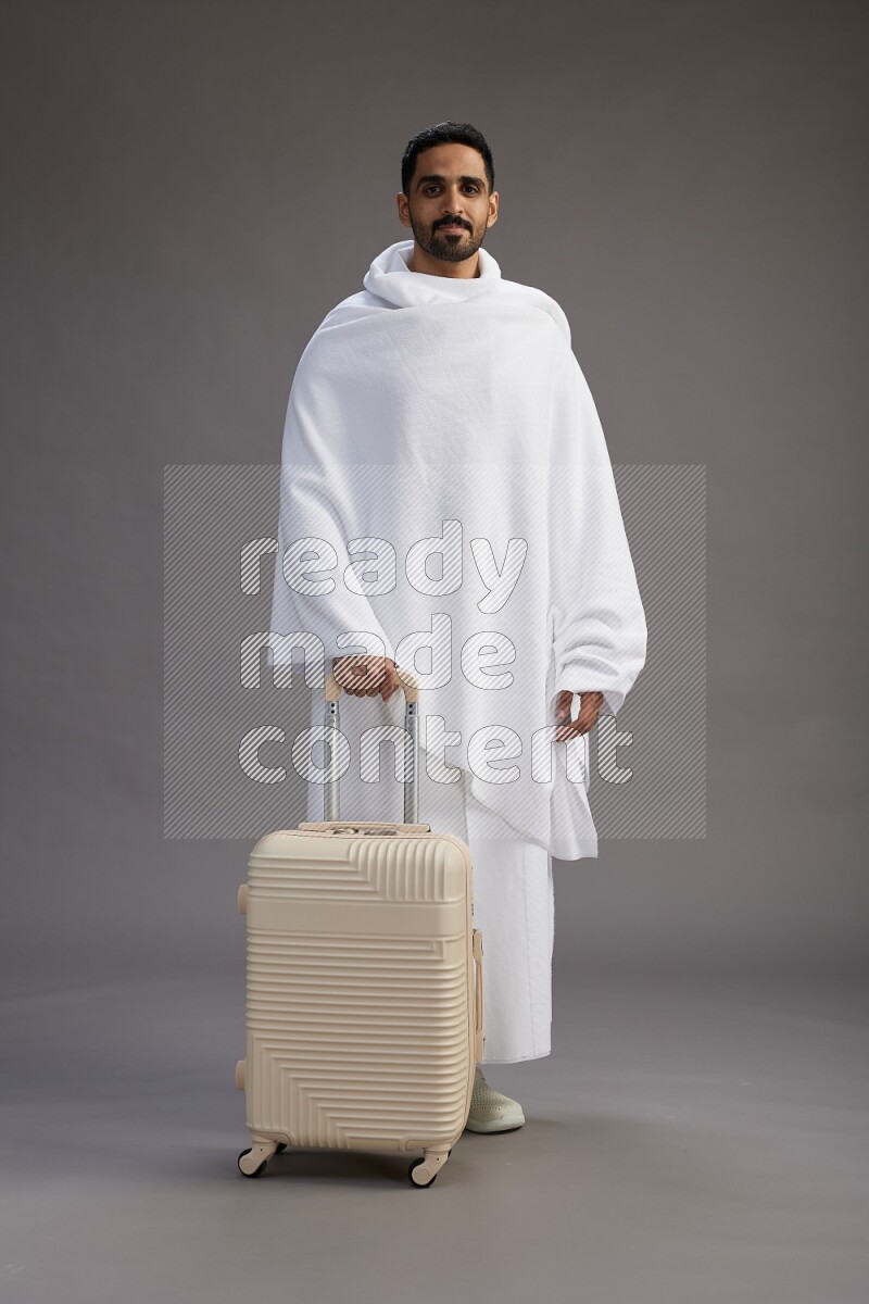 A man wearing Ehram Standing holding traveling bag on gray background