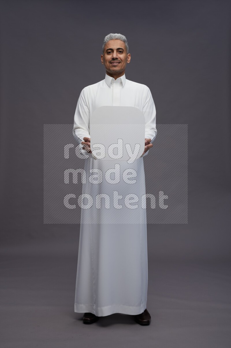 Saudi man wearing thob standing holding social media sign on gray background