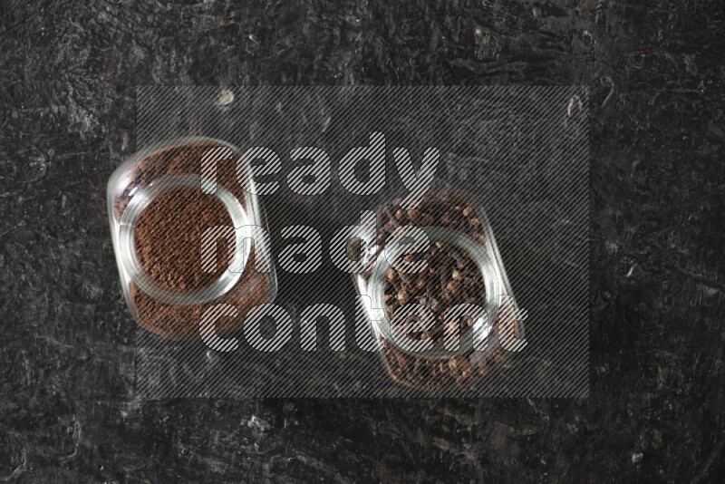 Glass spice jars full of cloves and cloves powder on textured black flooring