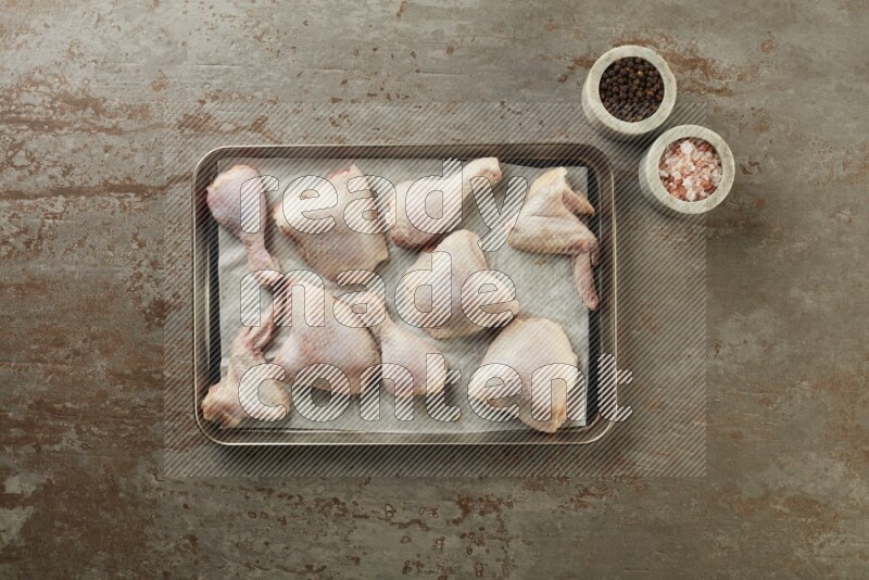 Mixed fresh chicken pieces in an oven tray on a textured rustic background