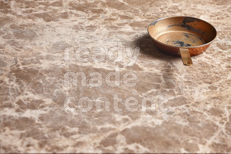 A small copper pan on beige marble background