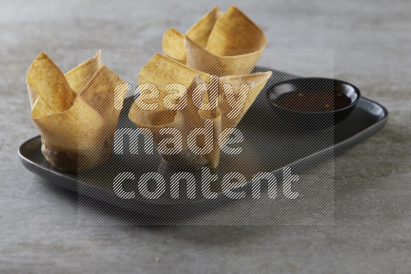 wonton cups with soy sauce ramkin on rectangle dark grey ceramic plate on grey textured counter top