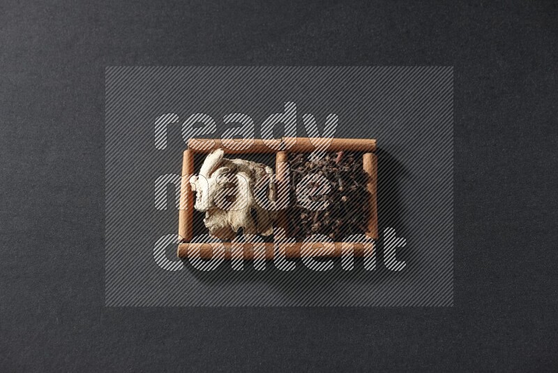 مربعان من أعواد القرفة ممتلئان بالقرنفل والزنجبيل المجفف علي خلفية سوداء