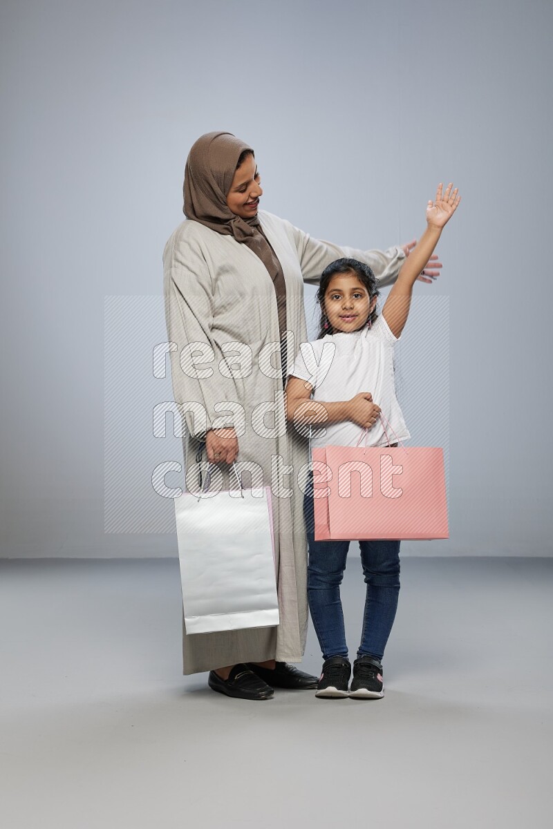 Mom and daughter holding shopping bags on gray background