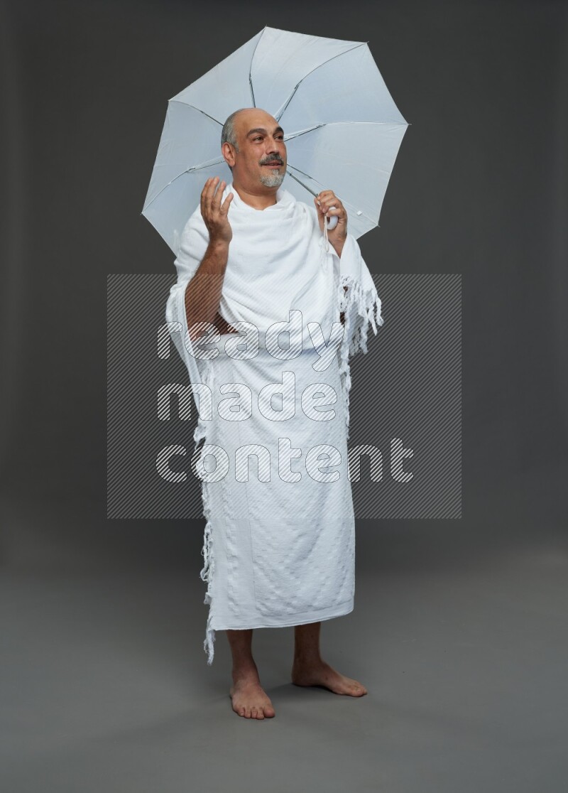 A man wearing Ehram Standing holding umbrella on gray background