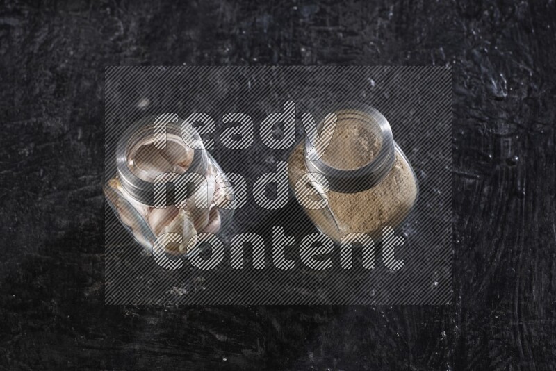 2 glass spice jars full of garlic powder and cloves on a textured black flooring
