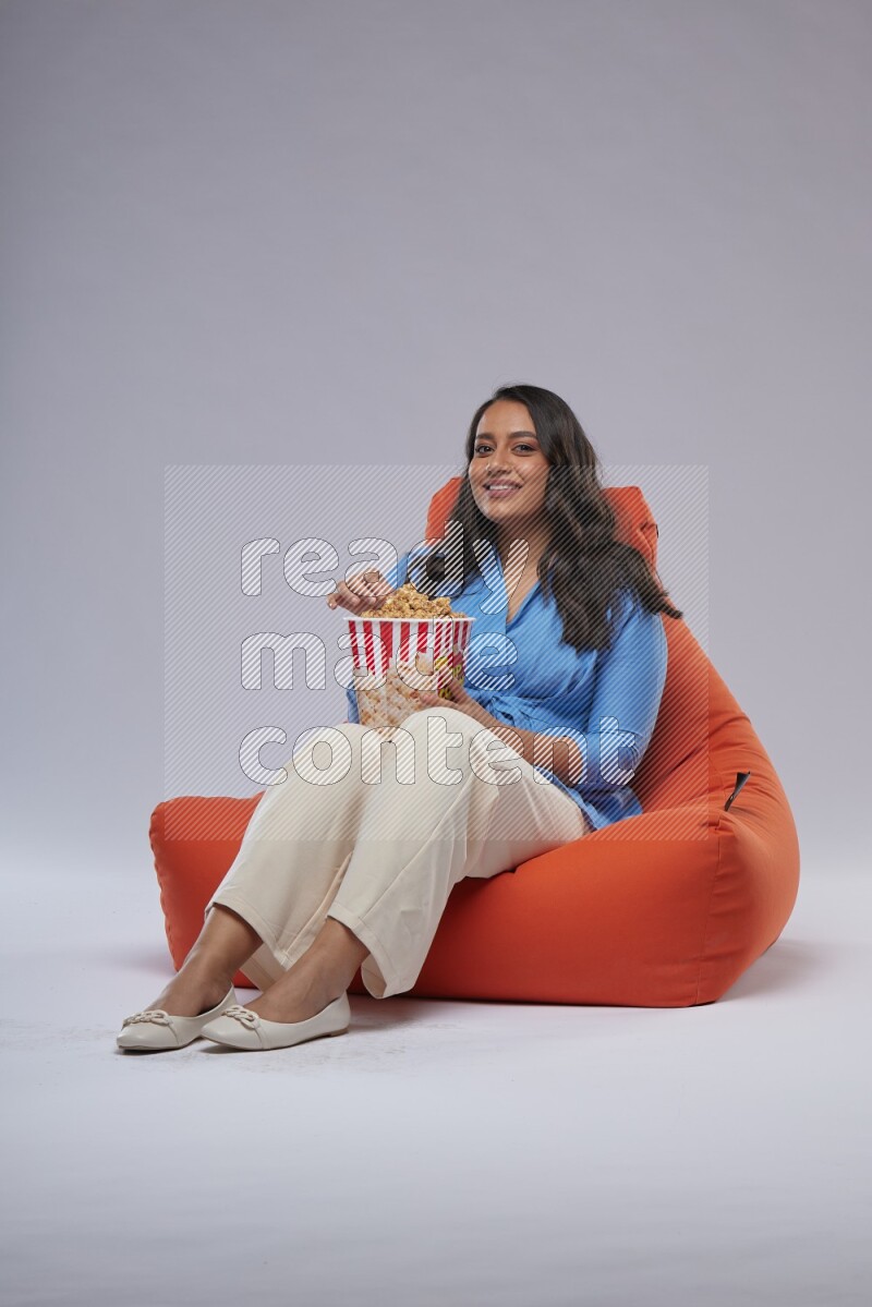A woman sitting on an orange beanbag and eating popcorn