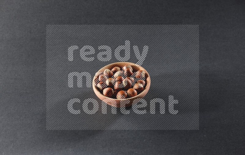 A wooden bowl full of hazelnuts on a black background in different angles