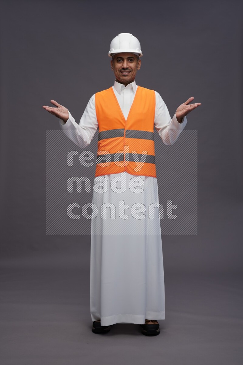 Saudi man wearing thob with engineer vest standing interacting with the camera on gray background