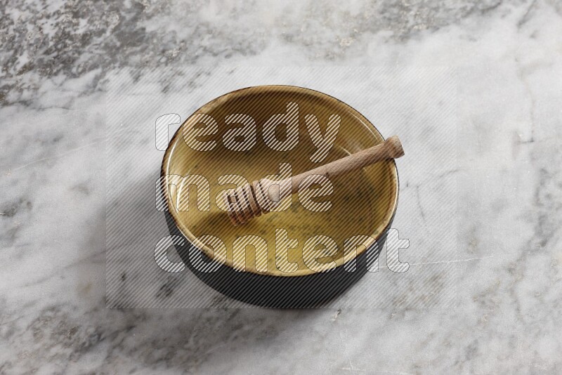 Multicolored pottery oven plate with wooden honey dipper in it on grey marble background