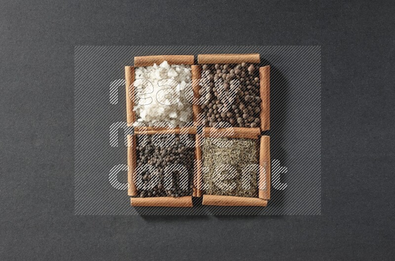 4 squares of cinnamon sticks full of black pepper, cumin, allspice and white salt on black flooring