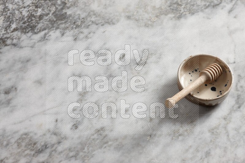 Multicolored pottery bowl with wooden honey dipper in it on grey marble background