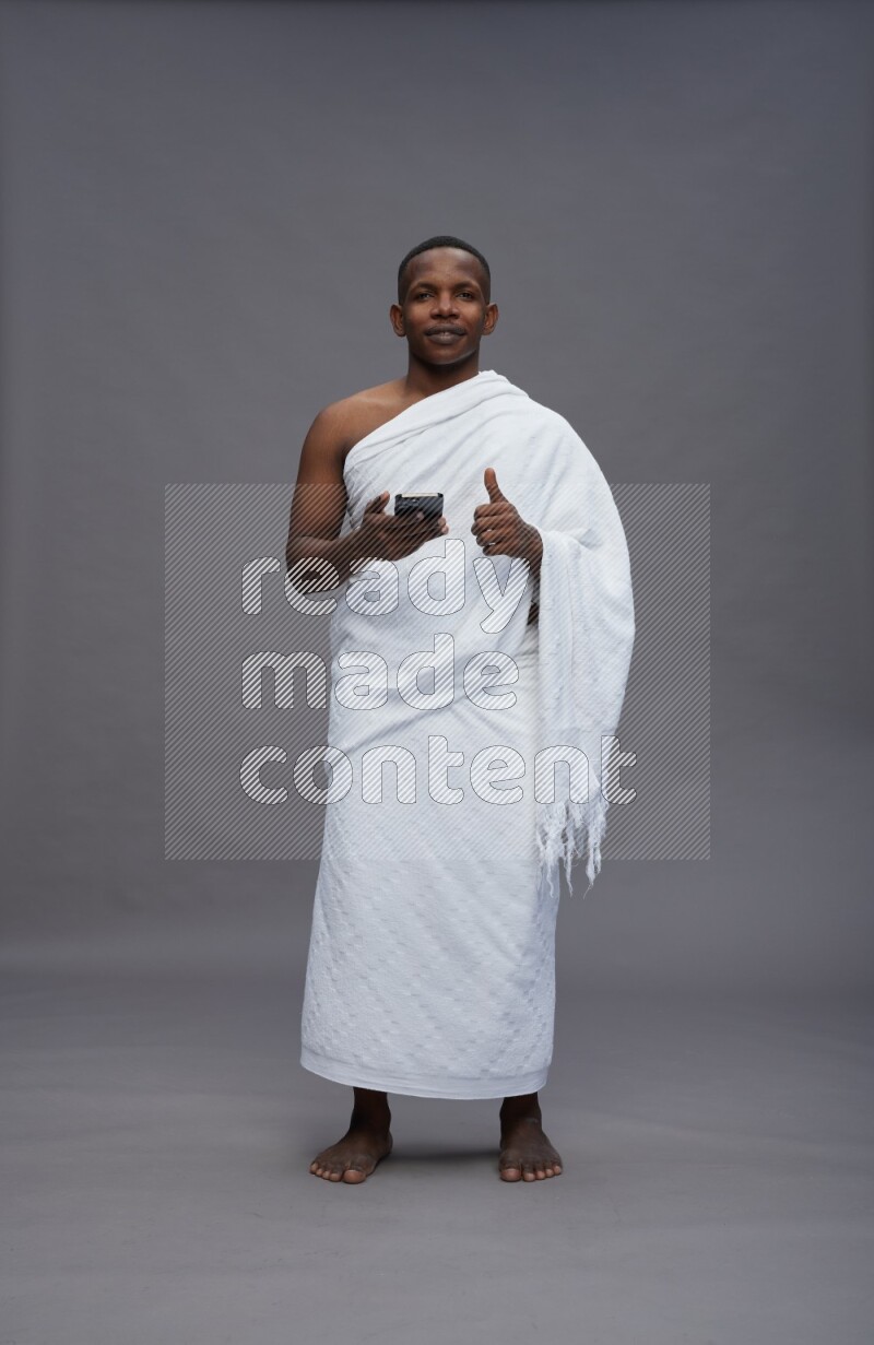 A man wearing Ehram Standing texting on phone on gray background