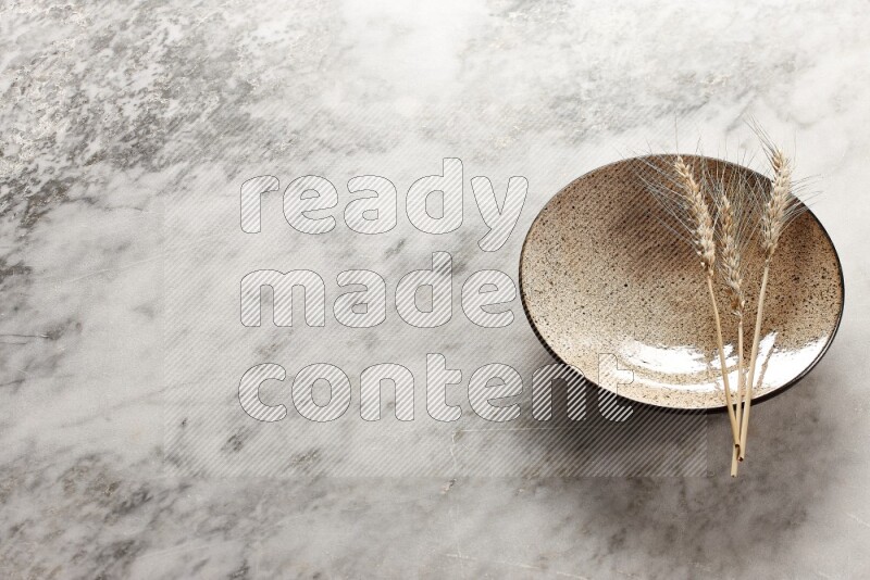 Wheat stalks on multicolored pottery plate on grey marble background