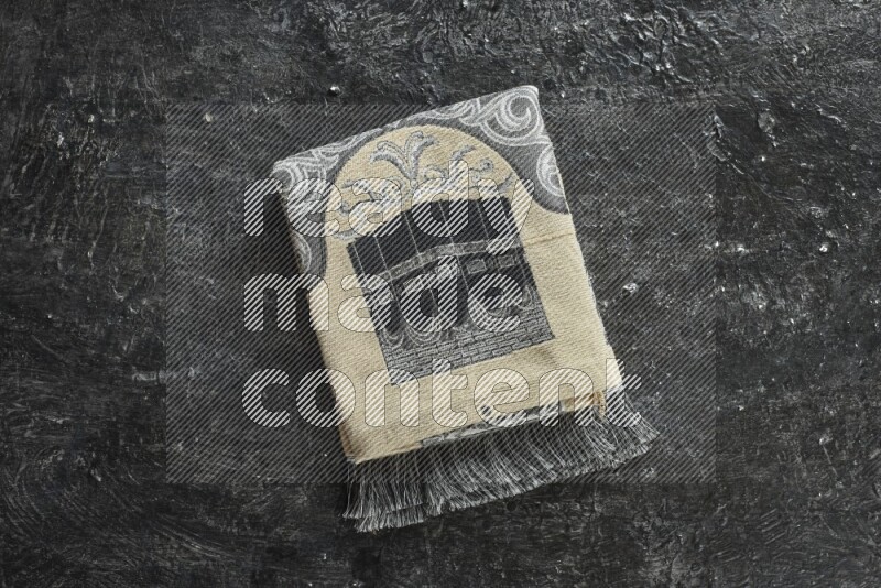 A folded prayer mat with different elements such as quran and prayer beads on black textured background