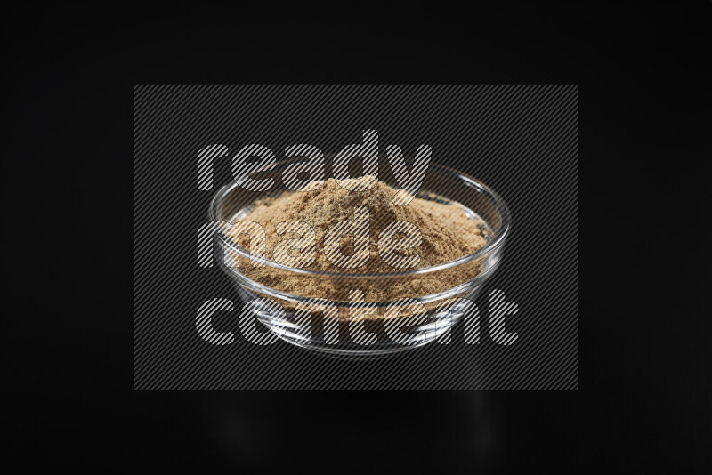 A glass bowl full of ground ginger powder on black background