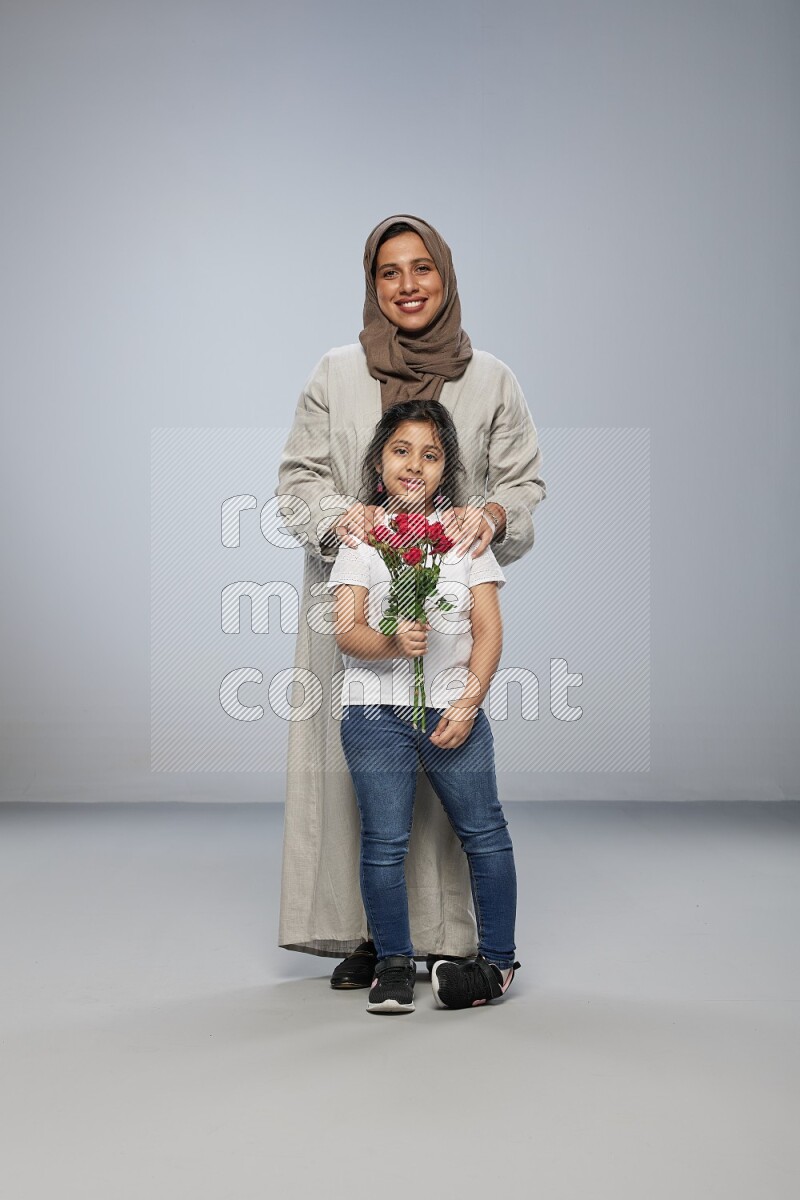 A girl standing giving flowers to her mother on gray background