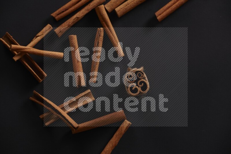 4 Cinnamon sticks stacked and bounded with more sticks in the background on black flooring