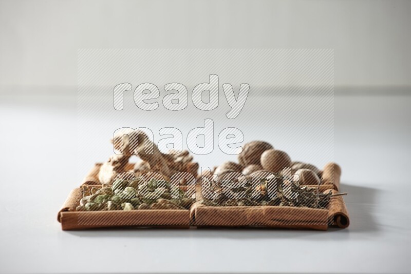 4 squares of cinnamon sticks full of nutmegs, dried ginger, cardamom and dried basil on white flooring