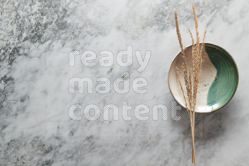 Wheat stalks on multicolored pottery plate on grey marble background