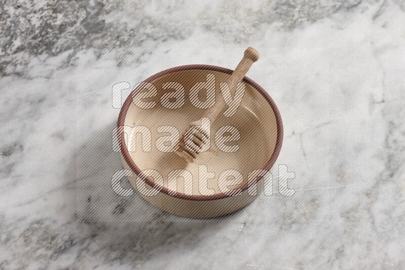 Beige Pottery oven bowl with wooden honey handle on the side with grey marble flooring, 65 degree angle