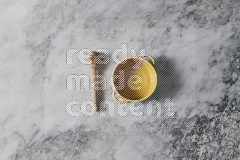 Multicolored pottery bowl with wooden honey dipper on the side on grey marble background