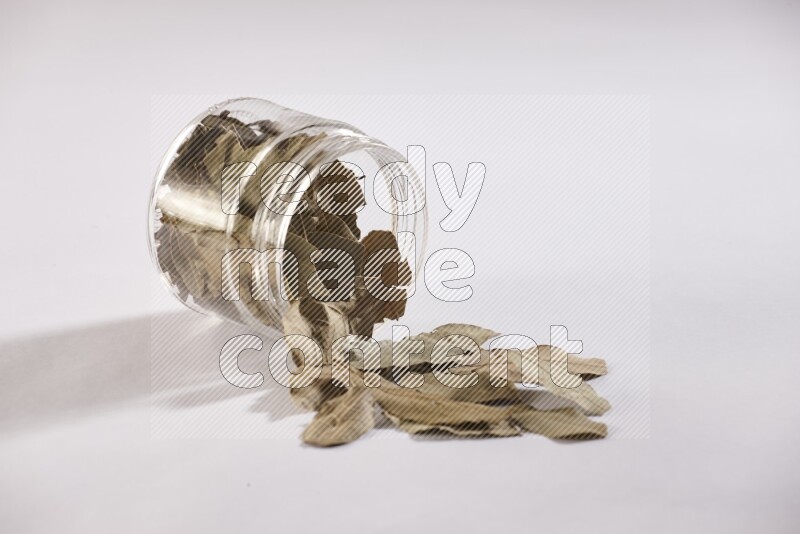 A glass jar full of dried bay leaves and jar is flipped and leaves spread out on white flooring