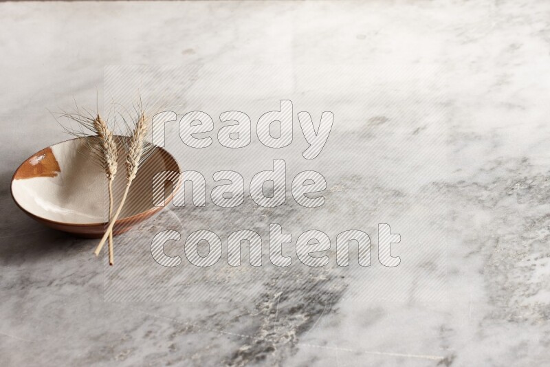 Wheat stalks on multicolored pottery plate on grey marble background
