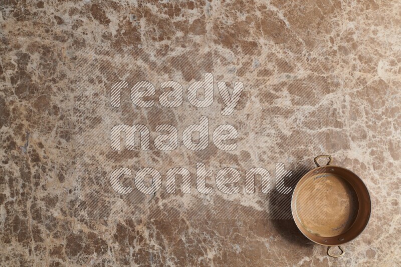A small copper pan on beige marble background