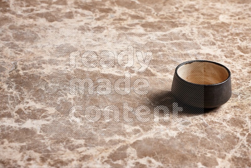 A black pottery bowl on beige marble background