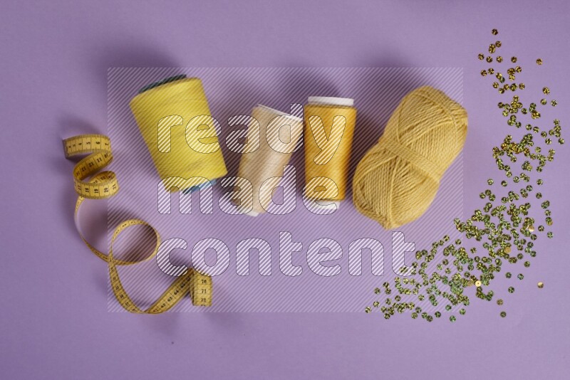 A yellow and purple collection of sewing and tailoring tools arranged on a purple background