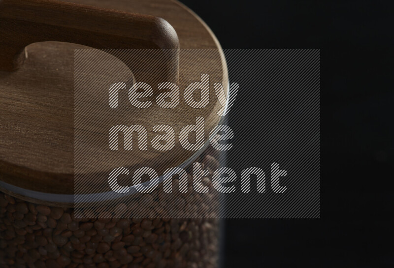Brown lentils in a glass jar on black background