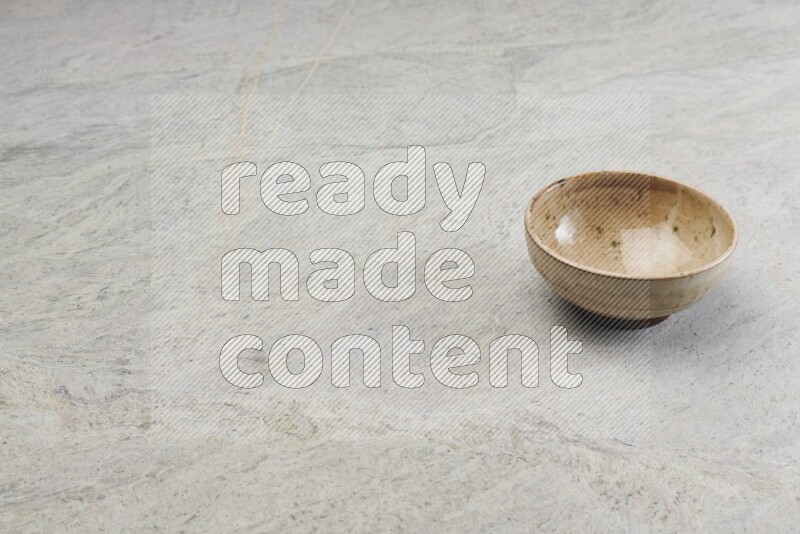 A small beige pottery bowl on grey marble background
