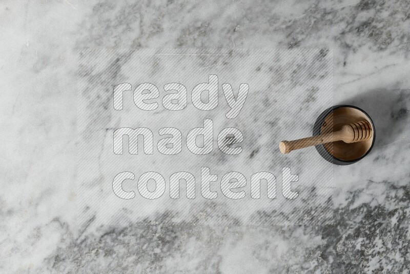 Black pottery bowl with wooden honey dipper in it on grey marble background