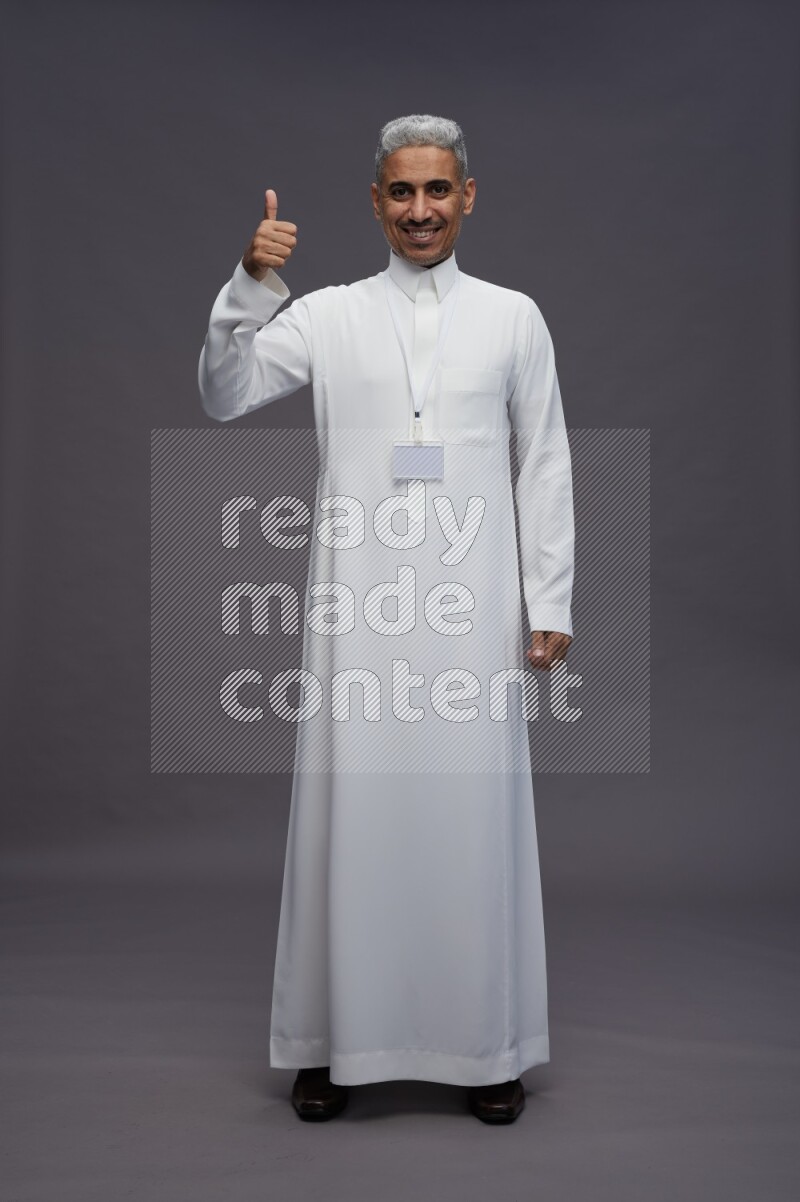 Saudi man wearing thob with neck strap employee badge standing interacting with the camera on gray background